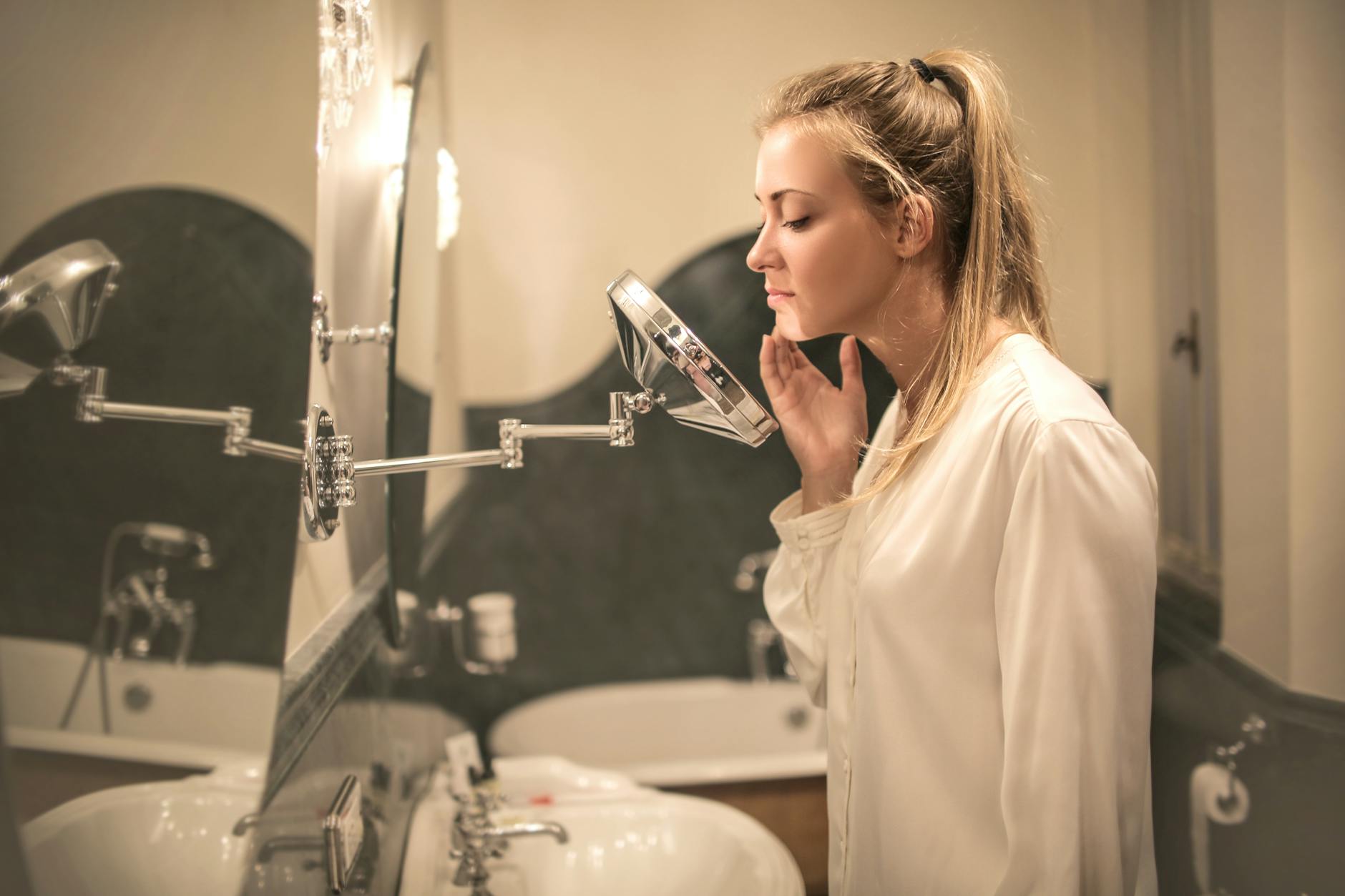 upset woman examining skin in small mirror